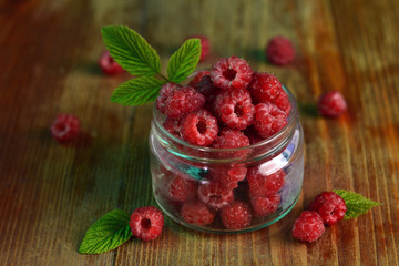 Bank with fresh raspberries on a wooden surface.