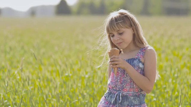Beautiful blond little girl eats ice-cream in the summer next to the wheat field. Warm sunny day.