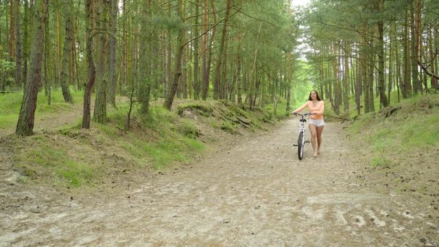 Young woman enjoying summer day in nature. Active girl walking with bicycle in forest park. Female tourist relaxing on fresh air, full HD.