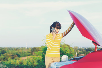 Obraz premium Young Woman in yellow sweater is calling to insurance for car roadside service and explaining her location because her car is dead between travel in vacation time.