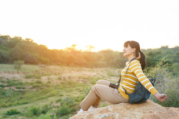 Naklejka na ściany i meble Young Woman in yellow sweater sitting on a giant rock for rest and stretching her arms for relax and breathing fresh air between travel in mountain for her vacation.