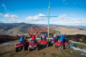 Group of people with raised hands up on red quad bikes near cross with a symbol of Ukraine on top...