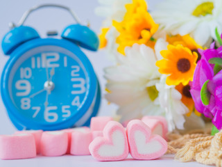 Closeup of sweet marshmallow in the shape of heart and Alarm clock on wooden plate and flower at background. Concept about time of love and relationship. (Soft Style for Background)