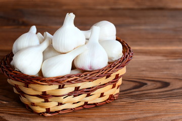 Raw whole garlic in a basket on a wooden background. Flavorful product, therapeutic food. Closeup