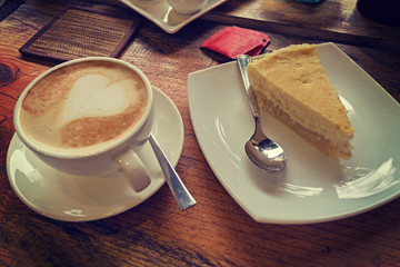 A cup of cappuccino with a heart pattern and a piece of cheesecake. Toned, instagram.