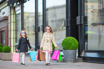 Adorable little girls with shopping bags walking in the city outdoors