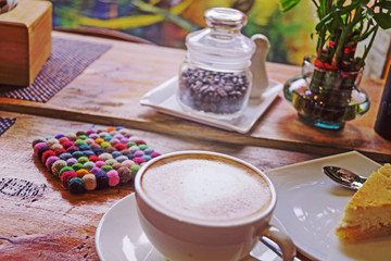 A cup of cappuccino with a heart pattern and a piece of cheesecake. Toned, instagram.