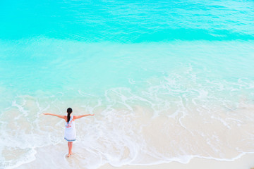 Young happy tourist girl at beach having a lot of fun in shallow water. Top view of a young girl and a snow-white beach with turquoise clean water.