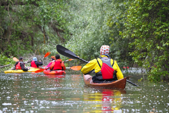 Group of people (friends) kayaking in wild river among thickets of plants on biosphere reserve in spring
