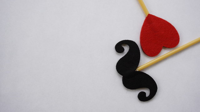 Top or flat lay view of Photo booth props red heart shape and a black mustache on a white background flat lay. Birthday parties and weddings.