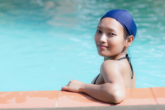 Girl in bikini and swimming cap leaning on the edge of the pool