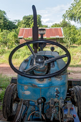 View of the interior of a used tractor with a steering wheel and the control board. Dirty old tractor parked under a shed on the farm