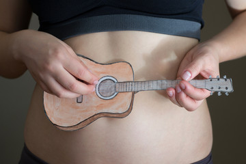 Women's hands hold a miniature paper guitar. Close up