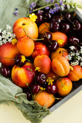 Cherries, apricots and peaches in a box on a yellow background