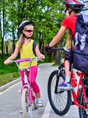 Fototapeta premium Bicycle path and sign with children. Girls wearing bicycle helmet with rucksack ciclyng ride. Kids are on white bike lane. Alternative to urban transport. Oncoming traffic. Unexpected meeting of two