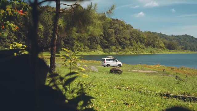 Camper van standing on a lake surrounded by hills, slide from bushes