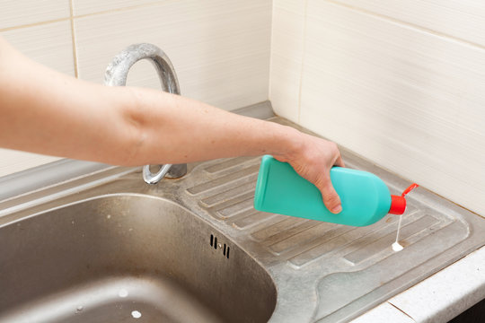 Woman hands with bottle of cleaning detergent for metal sink in the kitchen
