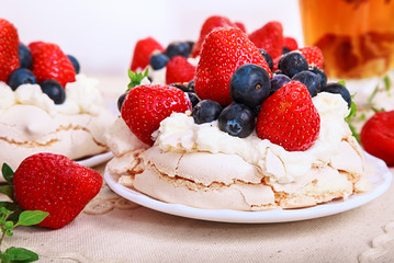 Pavlova is a meringue-based dessert with a crisp crust topped with strawberry and blueberry and whipped cream.
