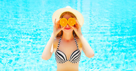 Summer sunny portrait woman holds in hands oranges hides his eyes on blue water pool background