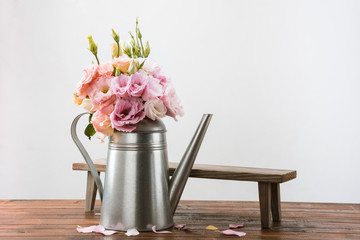 Close-up view of beautiful pink flowers in watering can and small wooden bench on table top