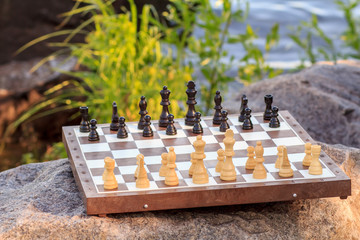 Chess board with chess pieces on rock with river embankment background