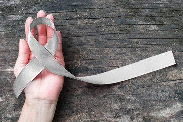 Silver color ribbon on hand support and ols aged wood (isolated with clipping path) for Parkinson's disease awareness and Brain cancer tumor illness