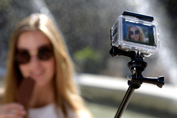 Junge Frau mit Eiscreme macht ein Selfie mit einer Actioncamera vor einem Brunnen