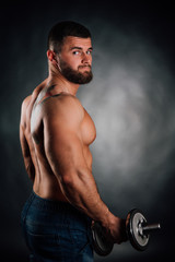 Fototapeta na wymiar Portrait of a bearded man fitness model, torso. Dumbbell in hand, view from back. Gray background.