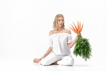 Beautiful blond woman  holding fresh carrot with green leaves on white background. Health and Diet