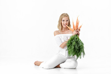 Beautiful blond woman  holding fresh carrot with green leaves on white background. Health and Diet