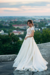 Fototapeta na wymiar Young girl in wedding dress on city background at sunset.