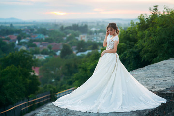 Fototapeta premium Young girl in wedding dress on city background at sunset.