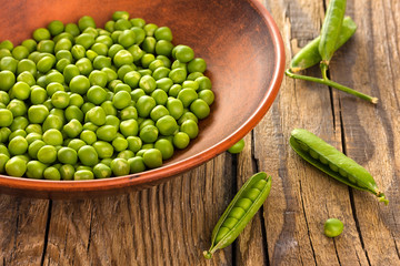Green peas in ceramic bowl on wooden background