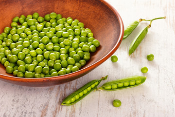 Green peas in ceramic bowl on wooden background