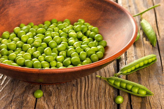 Green peas in ceramic bowl on wooden background
