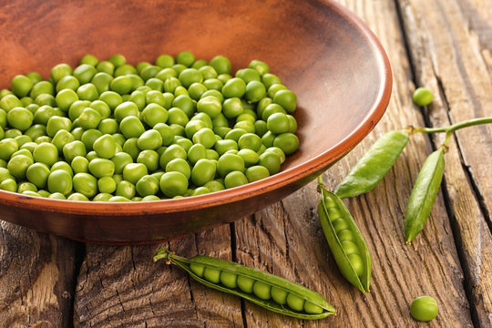Green peas in ceramic bowl on wooden background