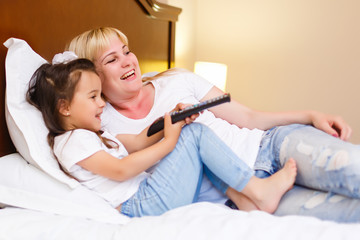happy mother with daughter in bed watching tv