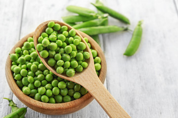 Bowl and spoon with fresh green peas on white wooden background