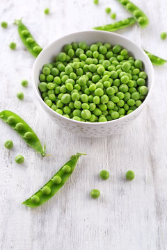 Bowl with fresh green peas on white wooden background