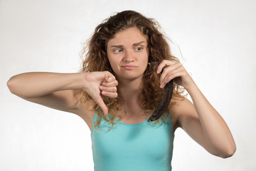 Fototapeta premium Beautiful curly girl holding a foul banana, looking at it and showing a thumbs-up on a background