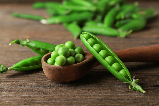 Wooden spoon with fresh green peas on table