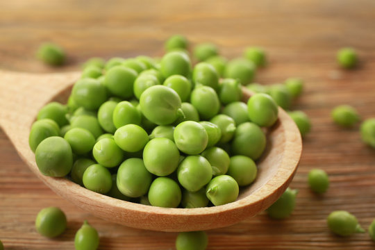 Wooden spoon with fresh green peas on table, closeup