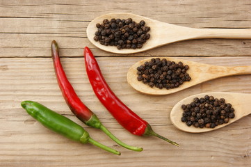 Black and red pepper in wooden spoon on the old board