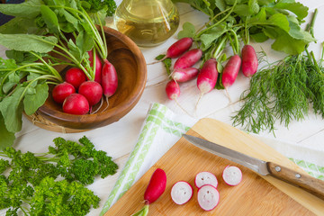 Olive oil, juicy fresh radish vegetables, cucumber and fragrant greens parsley, dill, lettuce ingredients for a vegetarian diet salad on a light background with copy space