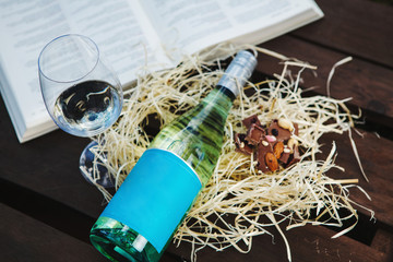Glass with white wine, bottle and chocolate near book