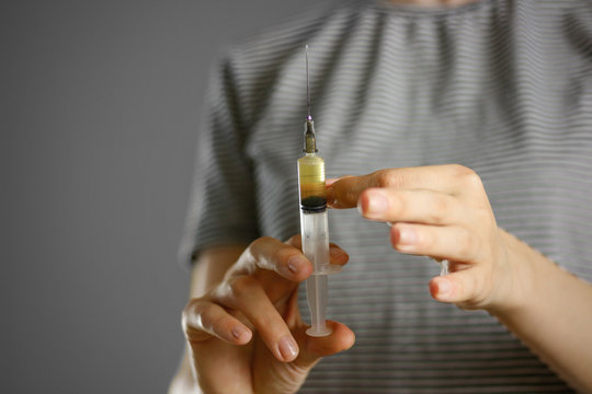 A young girl holding a syringe with a needle with the drug. Shakes off the bubbles. Closeup. Isolated on a grey background