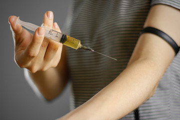 A young girl injects himself in the hand syringe with a needle with the drug. Closeup. Isolated on a grey background