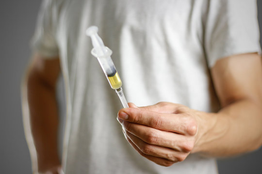 A young man holding a syringe with a needle with the drug. Closeup. Isolated on a grey background