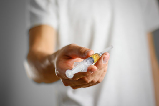 A young man holding a syringe with a needle with the drug. Closeup. Isolated on a grey background