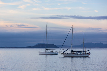 Two white yachts in marine bay near coastline of  Lanzarote island in cloudy morning, Canary Islands, Spain